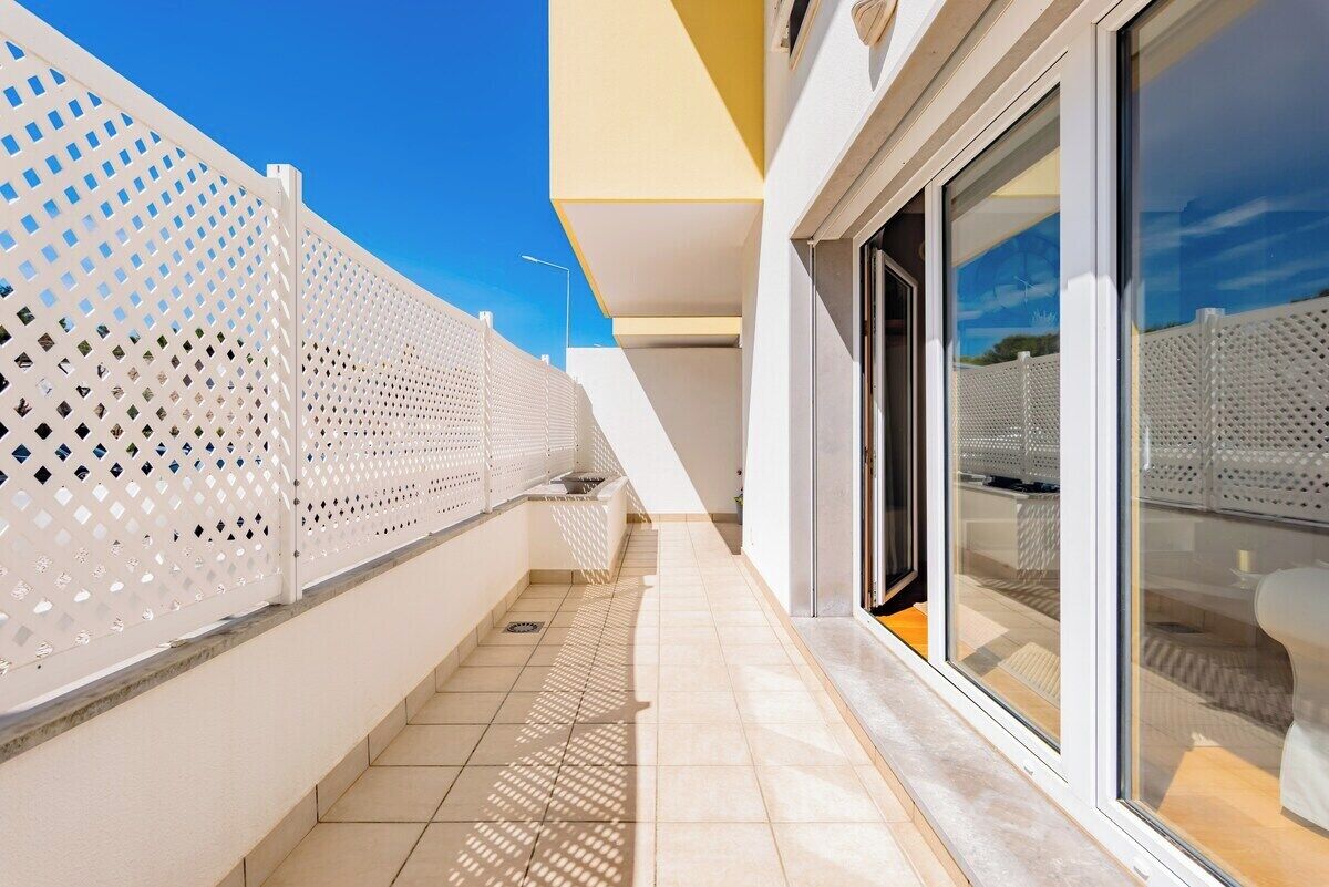 Un bâtiment moderne à l’extérieur blanc, doté d’un espace extérieur couvert et de grandes fenêtres.