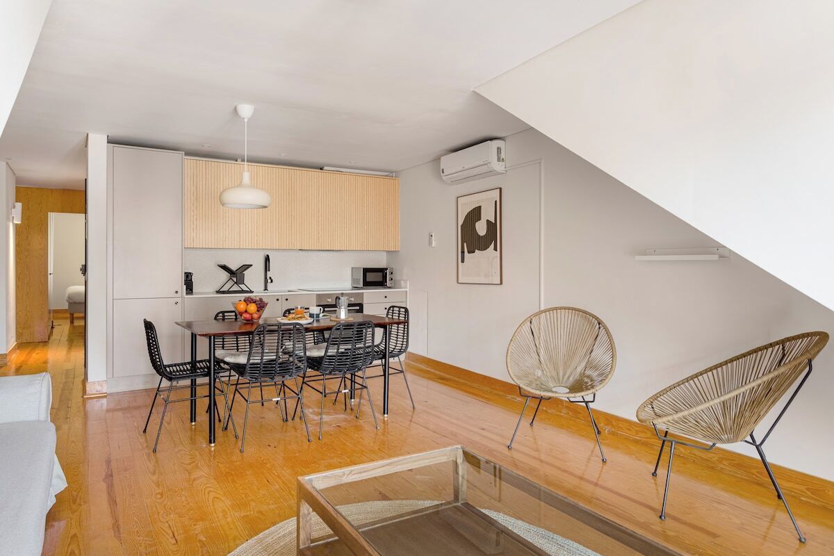 A modern kitchen with white cabinets, a dining area with a table and chairs, and a loft bedroom with a sloped ceiling.