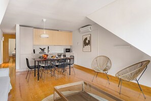 A modern kitchen with white cabinets, a dining area with a table and chairs, and a loft bedroom with a sloped ceiling. - Lapa River Loft Vibes (Cacilhas)