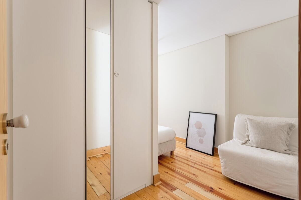 A room with a wooden floor, a white sofa, a bed, and a framed picture on the wall.