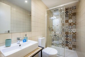 Ein Badezimmer mit großem Spiegel, weißem Waschbecken, Toilette und Dusche mit gemusterten Fliesen.