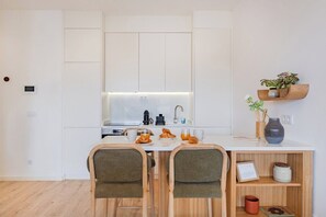 A modern kitchen with white cabinetry, a built-in oven, a coffee machine, and a breakfast setup with croissants and orange juice. - The Bright Life @ BoaVista Flats (Porto)