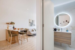 A modern kitchen with a dining area, a round mirror with lighting, and a minimalist design. - The Bright Life @ BoaVista Flats (Porto)
