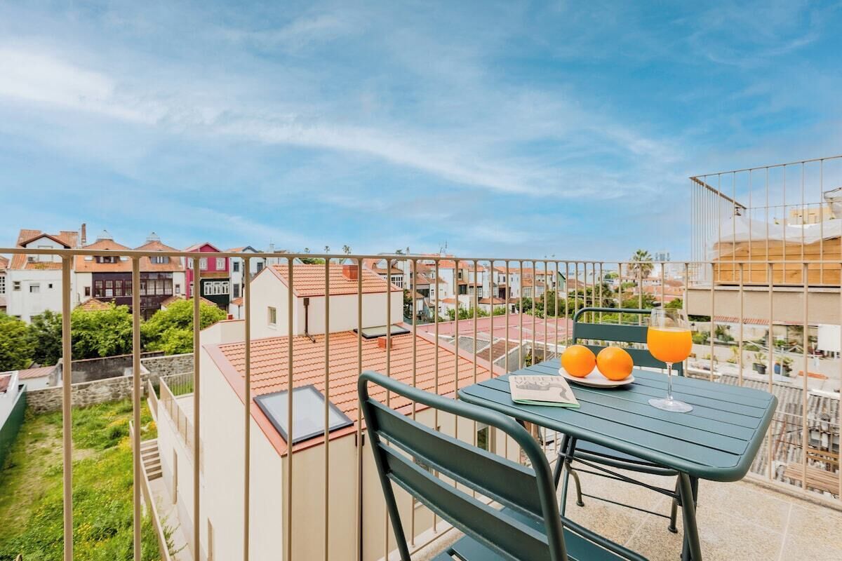 Een balkon met een tafel, twee stoelen, een boek en twee glazen sinaasappelsap.