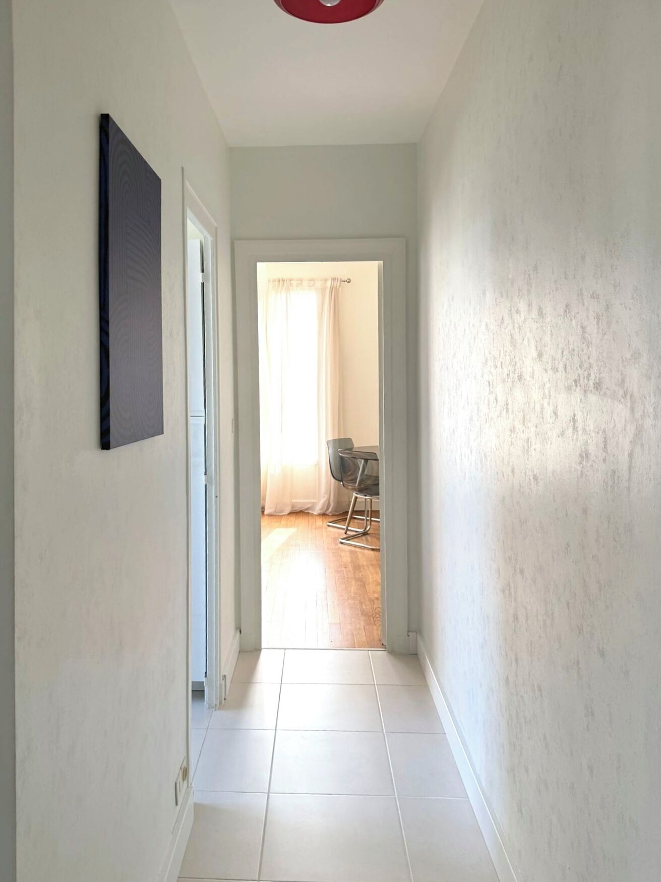 A hallway with a door leading to a room with a chair and a table.