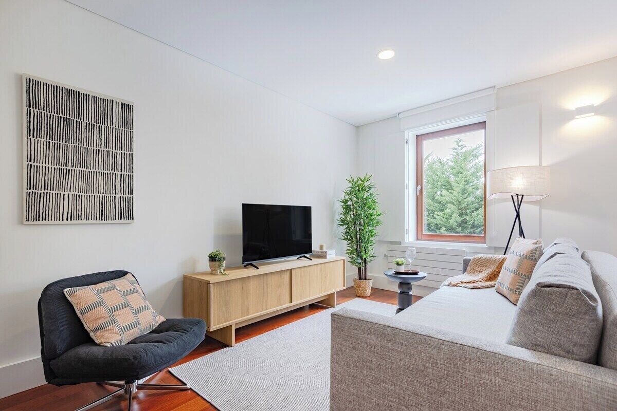 A modern living room with a TV, sofa, chair, and a potted plant.