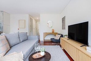 Ett modernt vardagsrum med en grå soffa, ett TV-bord i trä, en rund spegel och ett litet sidobord med ett glas och en växt.