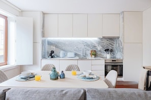 A modern kitchen with white cabinetry, a marble backsplash, and a dining area with a table set for breakfast. - 1BR with Balcony | Porto Urban Flats (Porto)
