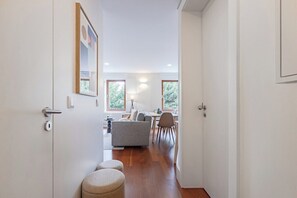 Een gang die uitkomt in een woonruimte met een bank, eettafel en stoelen.