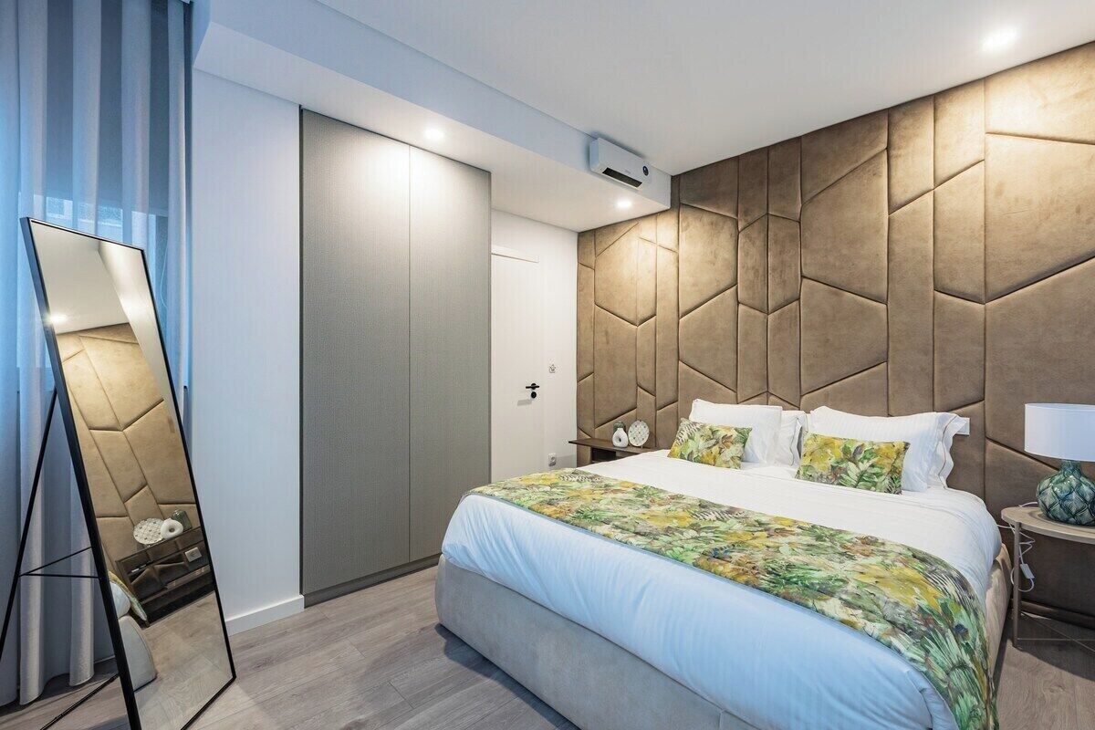 A modern hotel room with a large bed, a mirror, a nightstand, and a wardrobe.