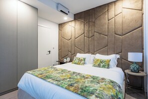 A hotel room with a bed, a nightstand with a lamp, a wall with a geometric pattern, and a door. - Arte do Azulejo @ Boavista Executive Studios (Porto)
