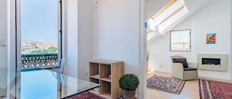 A modern living room with a glass table, a potted plant, a sofa, and a fireplace.