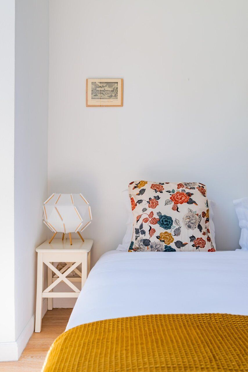 A bedroom with a bed, a small white nightstand, a framed picture on the wall, and a yellow blanket on the bed.