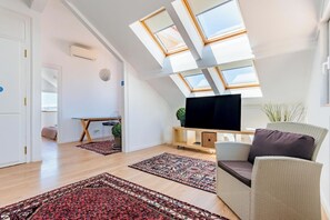 A spacious living area with skylights, a flat-screen TV, a sofa, and a dining table. - Costa do Castelo Sky Views (Lisbon)