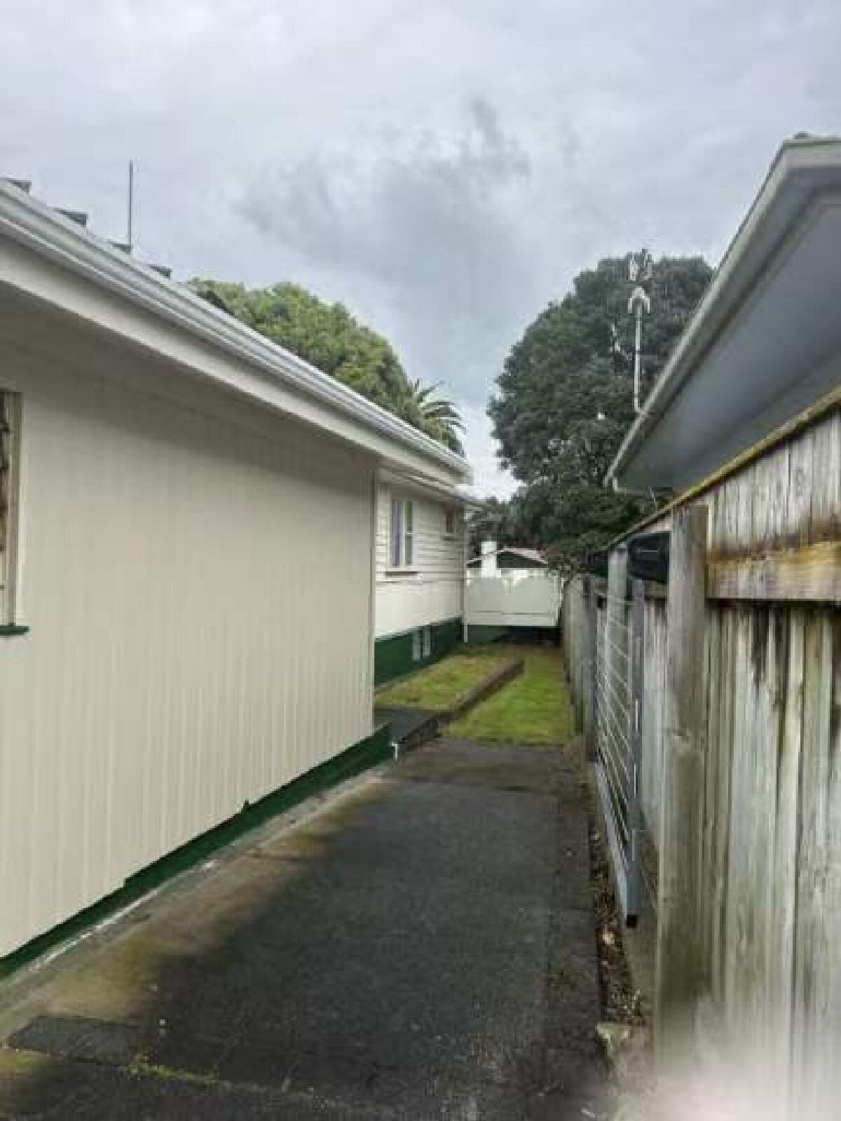 A narrow pathway between two buildings with a metal fence on one side and a wooden fence on the other.