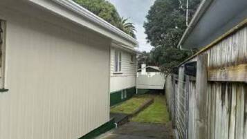 A narrow pathway between two buildings with a metal fence on one side and a wooden fence on the other.