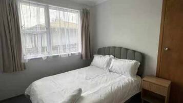 Una habitación de hotel con una cama, una mesita de noche, un armario de madera y una ventana con cortinas.