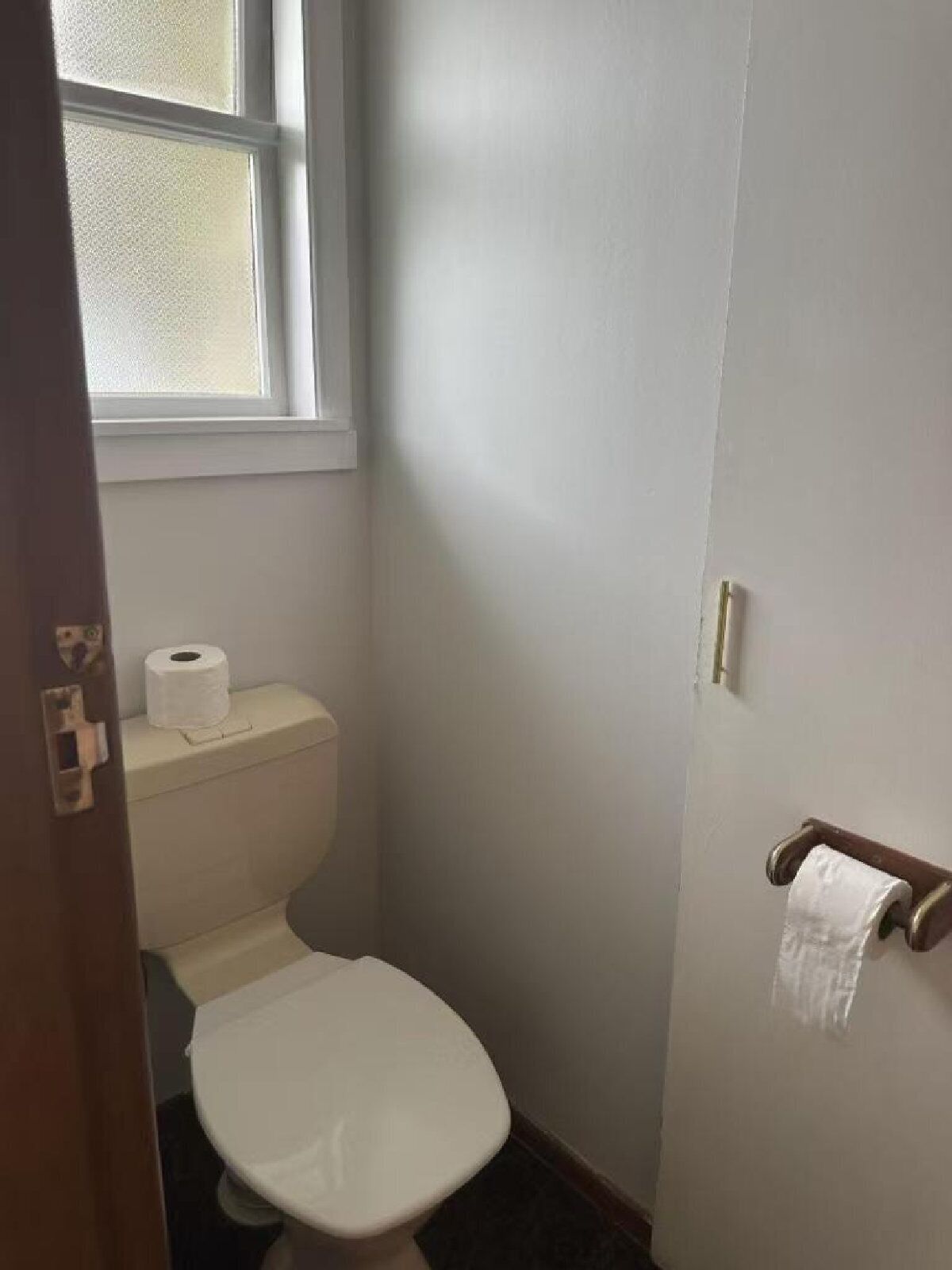 Um banheiro pequeno e estreito, com vaso sanitário, um rolo de papel higiênico no reservatório e um porta-toalhas na parede.