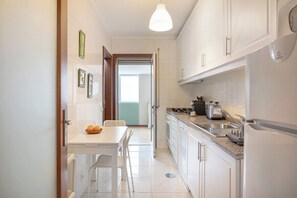 Een smalle keuken met witte kasten, een wit aanrecht, een spoelbak, een fornuis en een koelkast.