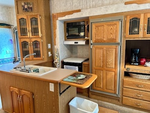Cocina compacta con armarios de madera, microondas, estufa y cafetera.