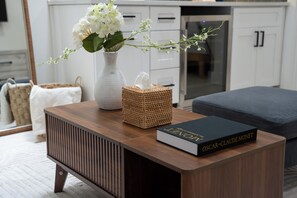 A modern kitchen with white cabinets, a wooden countertop, a vase with flowers, a book titled 'Oscar - Claude Monet,' and a wicker basket.