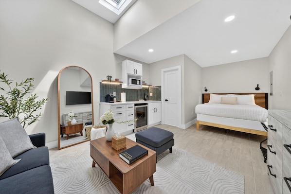 A modern bedroom with a bed, bedside tables, a mirror, and a small kitchenette.