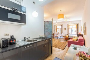 A modern kitchen with a built-in oven, a sink, and a toaster. There is a dining area with a red sofa and a table with a vase of flowers. - Rosarinho Cruz invites to her Atelier by the River (Porto)