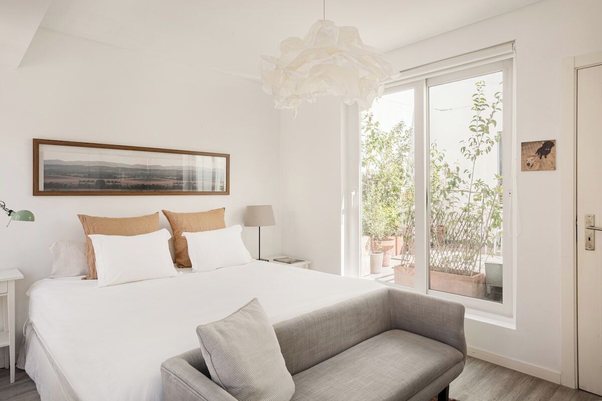 Un dormitorio con cama, sofá, un ventanal grande y una lámpara colgante.