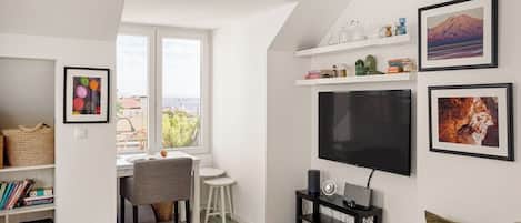 Una sala moderna con televisor de pantalla plana, un comedor con mesa y sillas, y una estantería.
