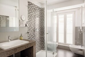 Een moderne badkamer met een douche met glazen wand, een grote spiegel, een wastafel en een toilet.