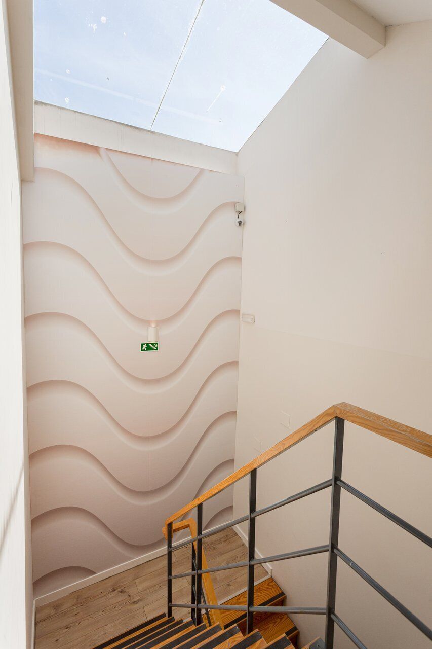Una escalera con diseño moderno, un tragaluz y una señal de salida de emergencia verde.