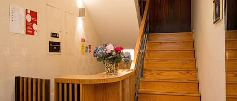 A reception desk with a wooden finish, a staircase with wooden steps, and a sign indicating the name of the establishment.