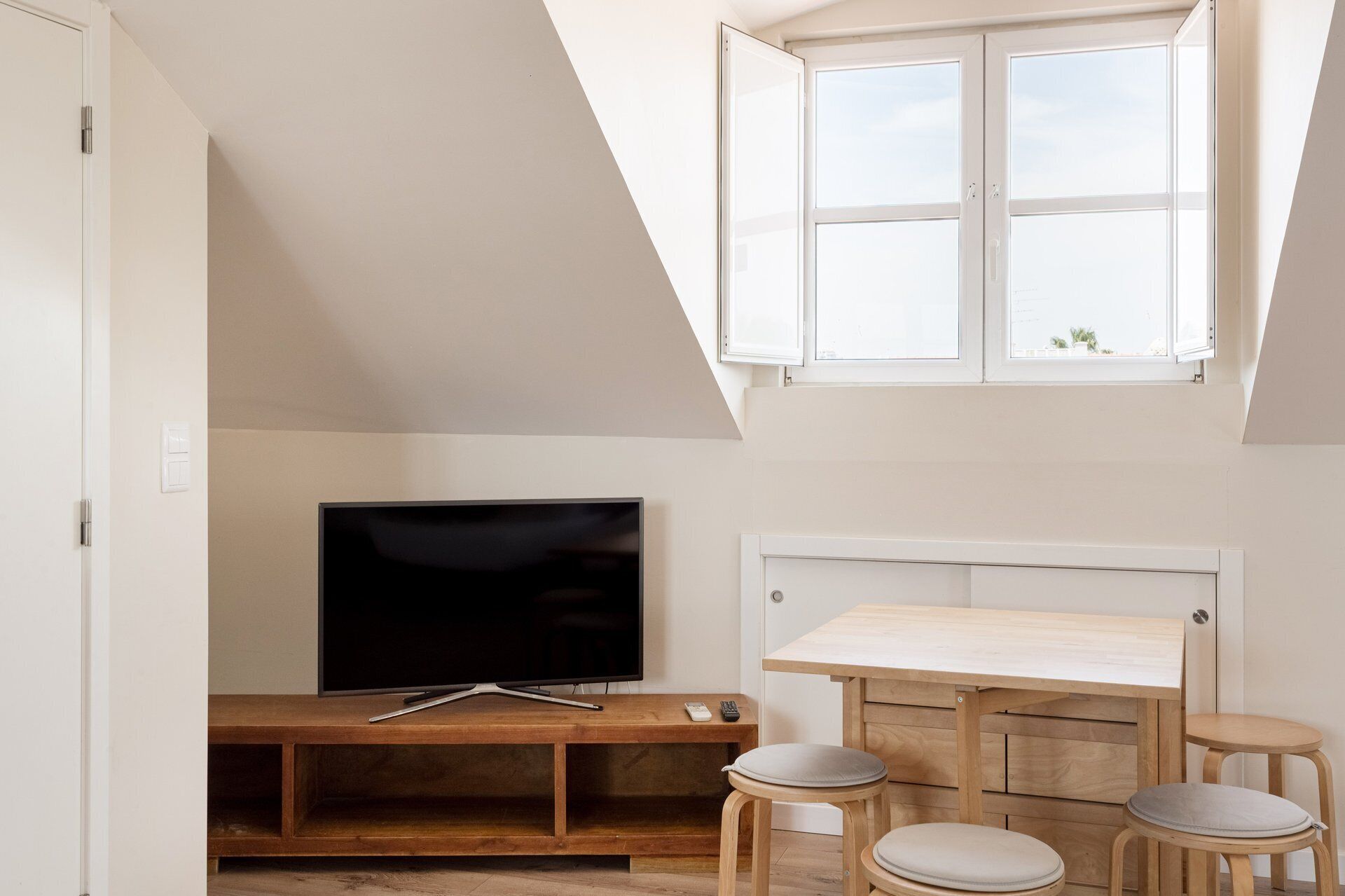 Una stanza con una TV su un mobile in legno, un tavolino con degli sgabelli e una finestra con vista.