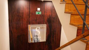Een trap met houten treden en metalen leuningen die leidt naar een donkerhouten deur met een bord waarop een gastenverblijf wordt aangegeven.