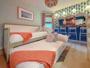 Een kamer met twee stapelbedden, een kitchenette met barkrukken, een spiegel en een ingelijste poster aan de muur.