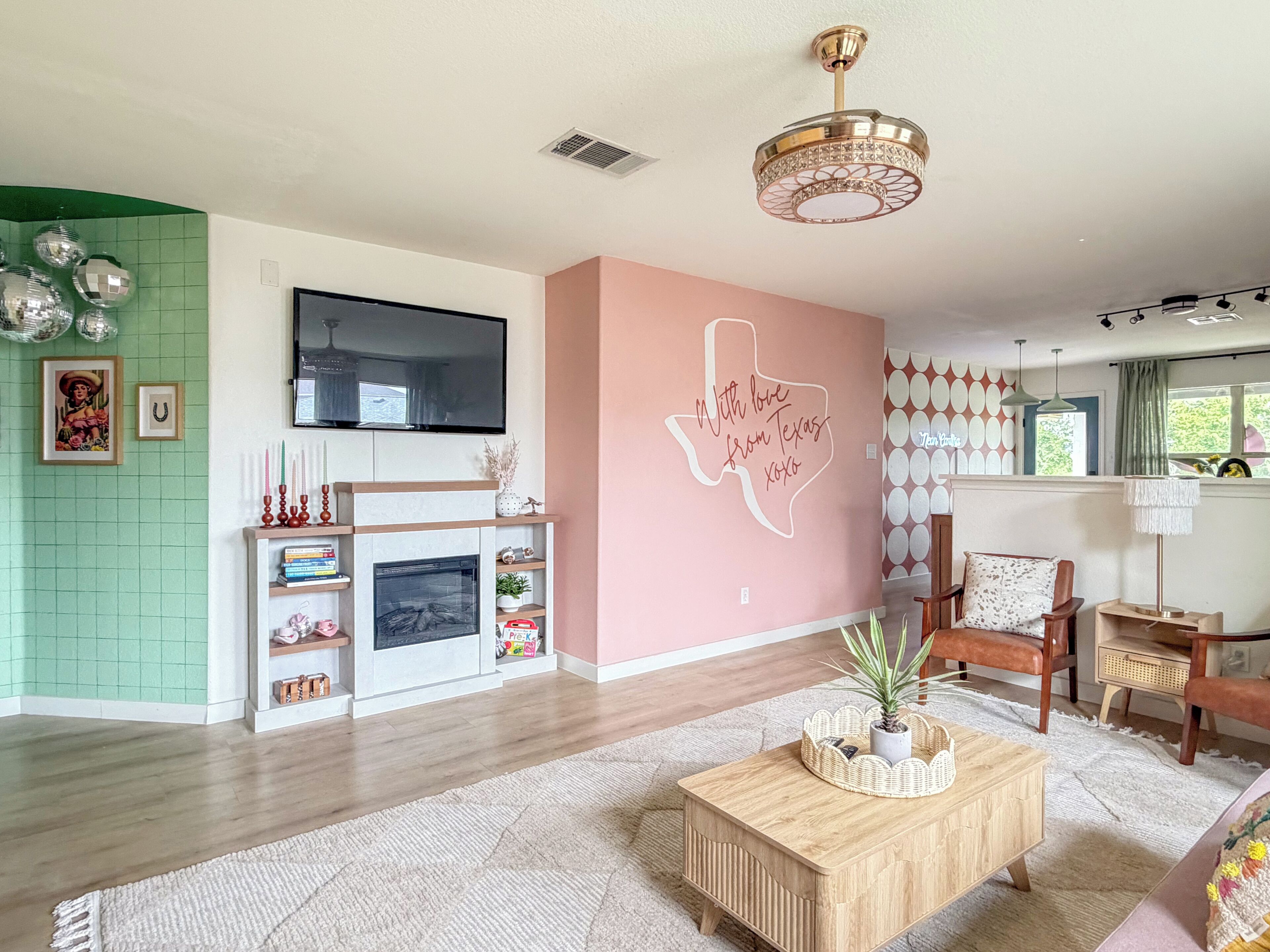 A living room with a fireplace, a television mounted on the wall, and a decorative wall with a Texas-themed design.