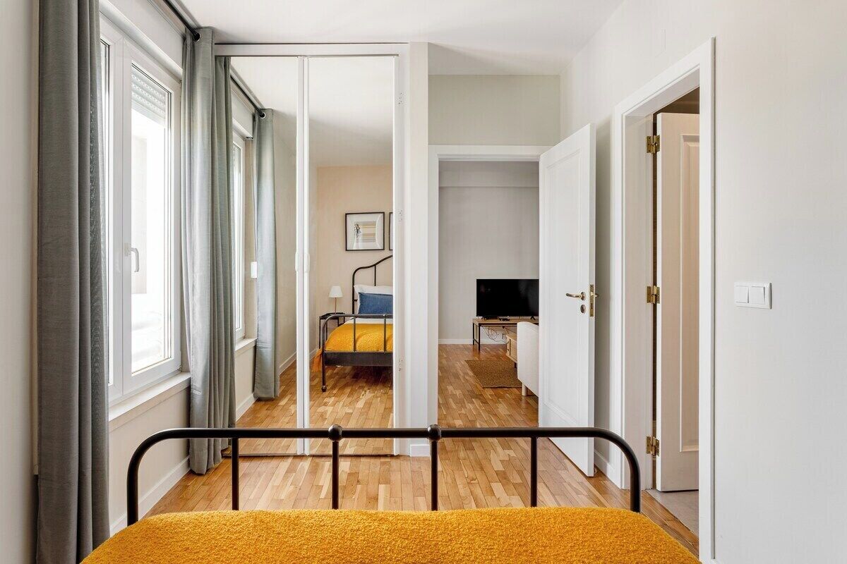 A narrow hallway with a bed, a television, and a door leading to another room.
