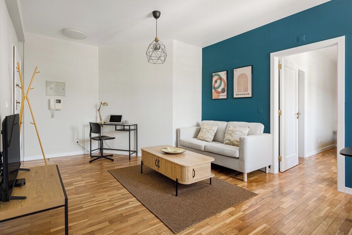 Ein modernes Wohnzimmer mit Couchtisch aus Holz, einer weißen Couch, einem Schreibtisch mit Computer und einer blauen Akzentwand.