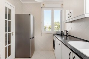 Una cocina compacta con un refrigerador de acero inoxidable, una lavadora y un ventanal con vistas a zonas verdes.