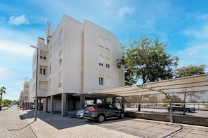 Un edificio moderno con una zona de estacionamiento techada y un coche estacionado frente a él.