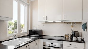 Een keuken met witte kastjes, een dubbele spoelbak, een magnetron en een fornuis.