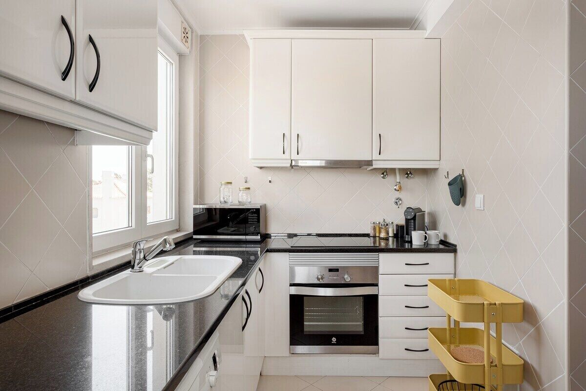 A modern kitchen with a double sink, stainless steel appliances, white cabinets, and a yellow storage cart.