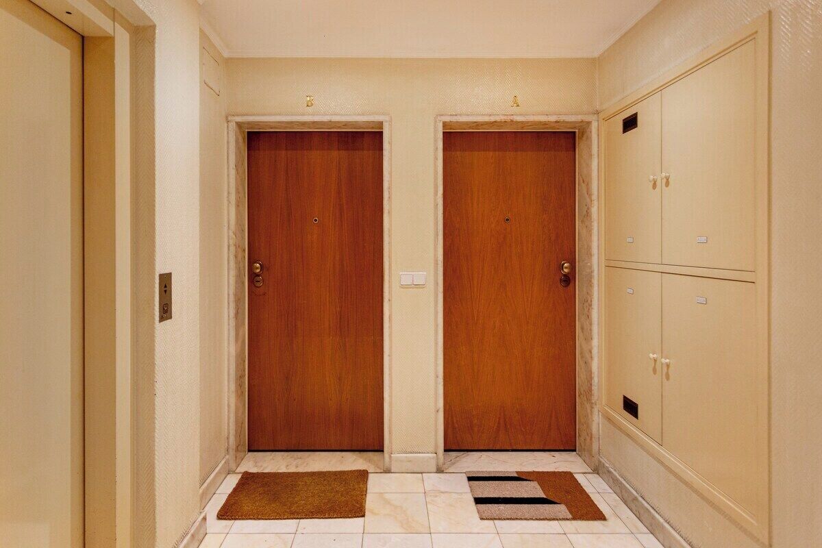 Un couloir avec deux portes en bois, un mur de couleur beige et un sol carrelé.