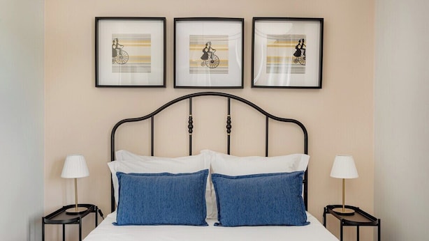 Een bed met hoofdeinde, twee kussens, een gele deken en een lijst met kunstwerk aan de muur.