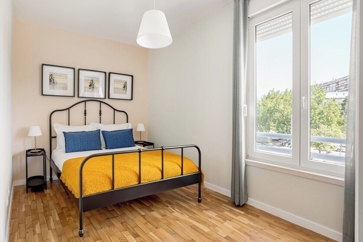 Une chambre à coucher comprenant un lit, des tables de chevet, des tableaux encadrés, une fenêtre avec vue et un luminaire suspendu.