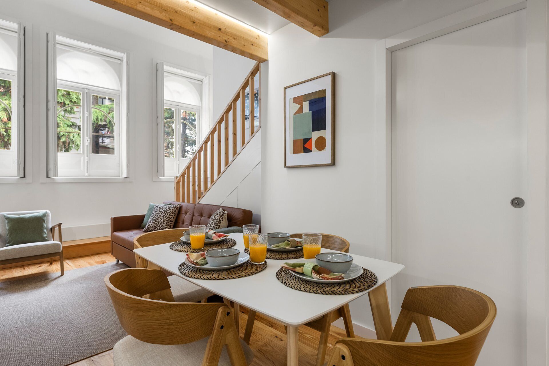 Un comedor con una mesa blanca, sillas de madera y una escalera.