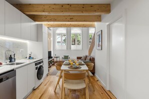 A modern kitchen with white cabinetry, a wooden ceiling, and a dining area with a table and chairs. - Porto Garden | Mezzanine Loft (Porto)