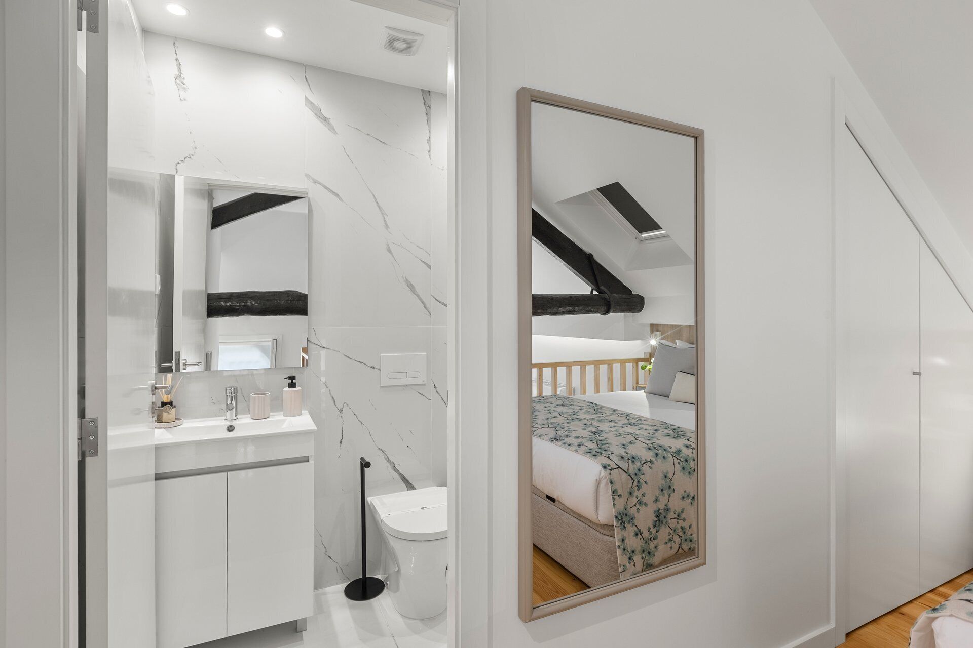 Un baño moderno con pared de mármol, un espejo grande y un inodoro.