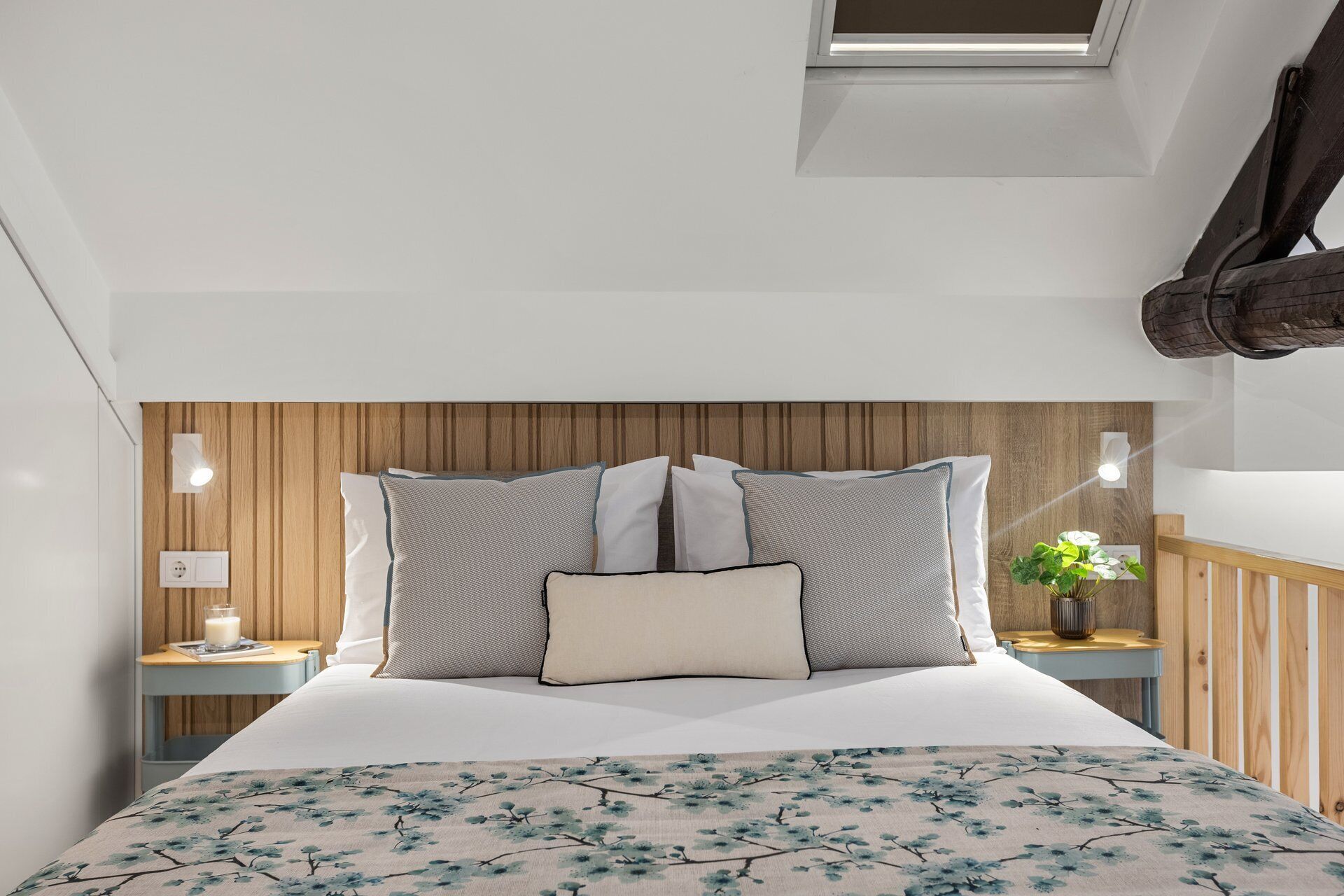 Una camera da letto con una testiera in legno, un letto con molti cuscini, comodini con lampade e un lucernario.