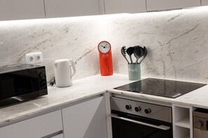 A kitchen with a microwave, kettle, clock, and utensil holder on a marble countertop. - Porto Garden | Mezzanine Loft (Porto)